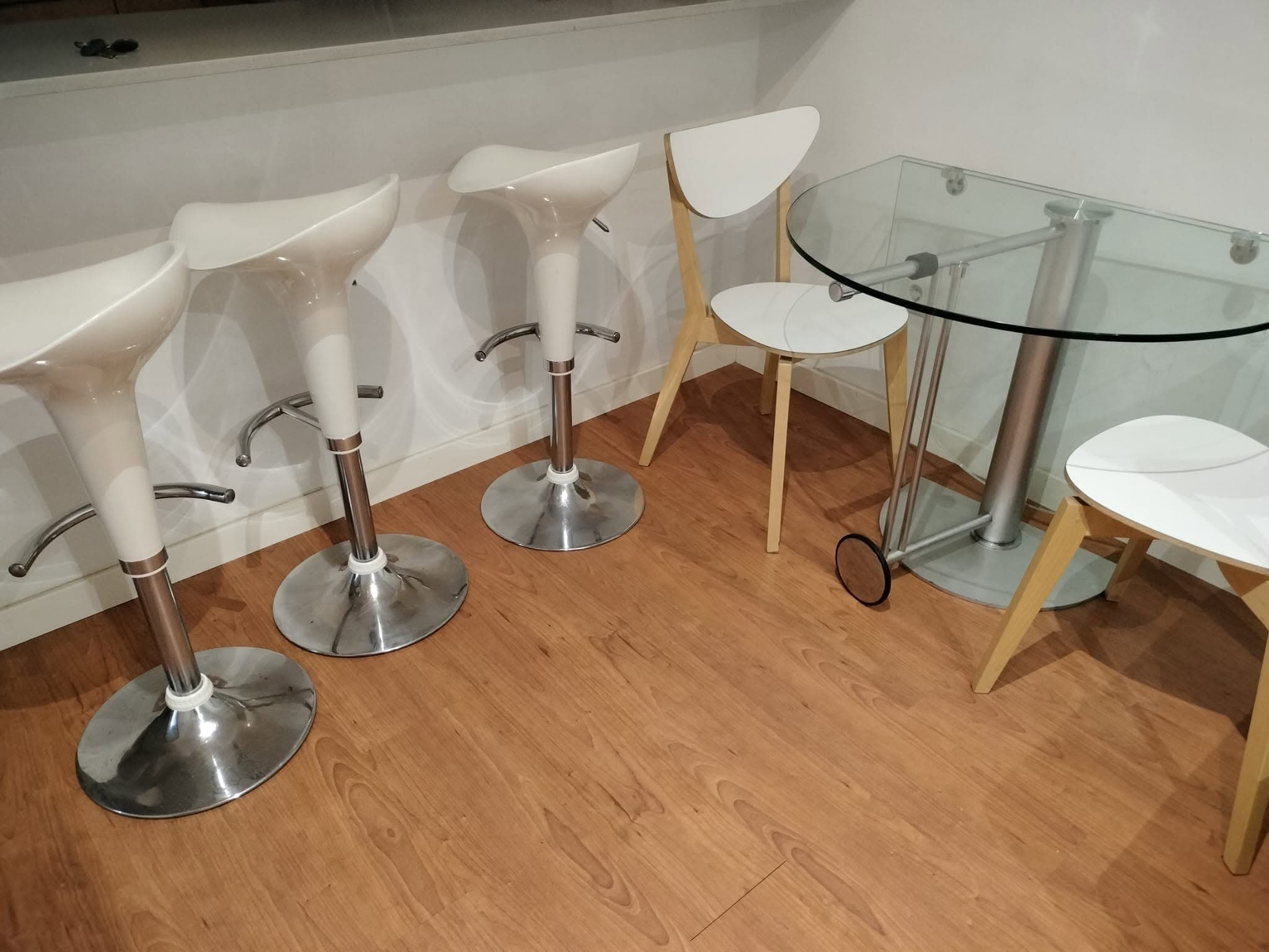 Taburetes blancos, sillas y mesa de cristal sobre suelo de madera, limpios
